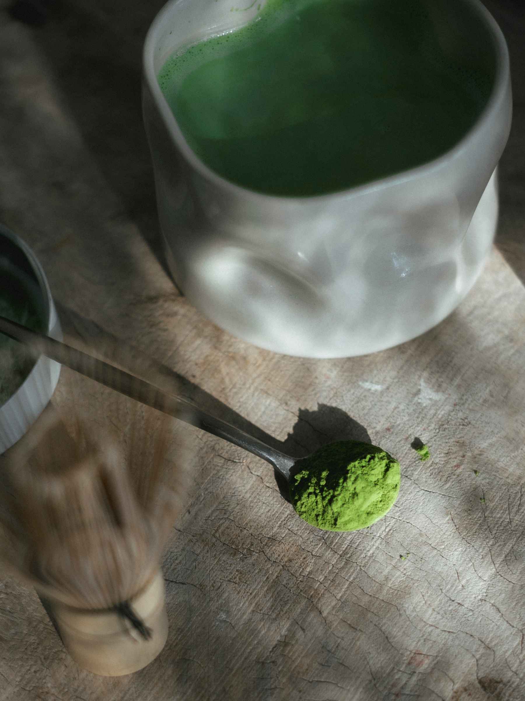 Matcha green tea powder with a whisk on a wooden surface
