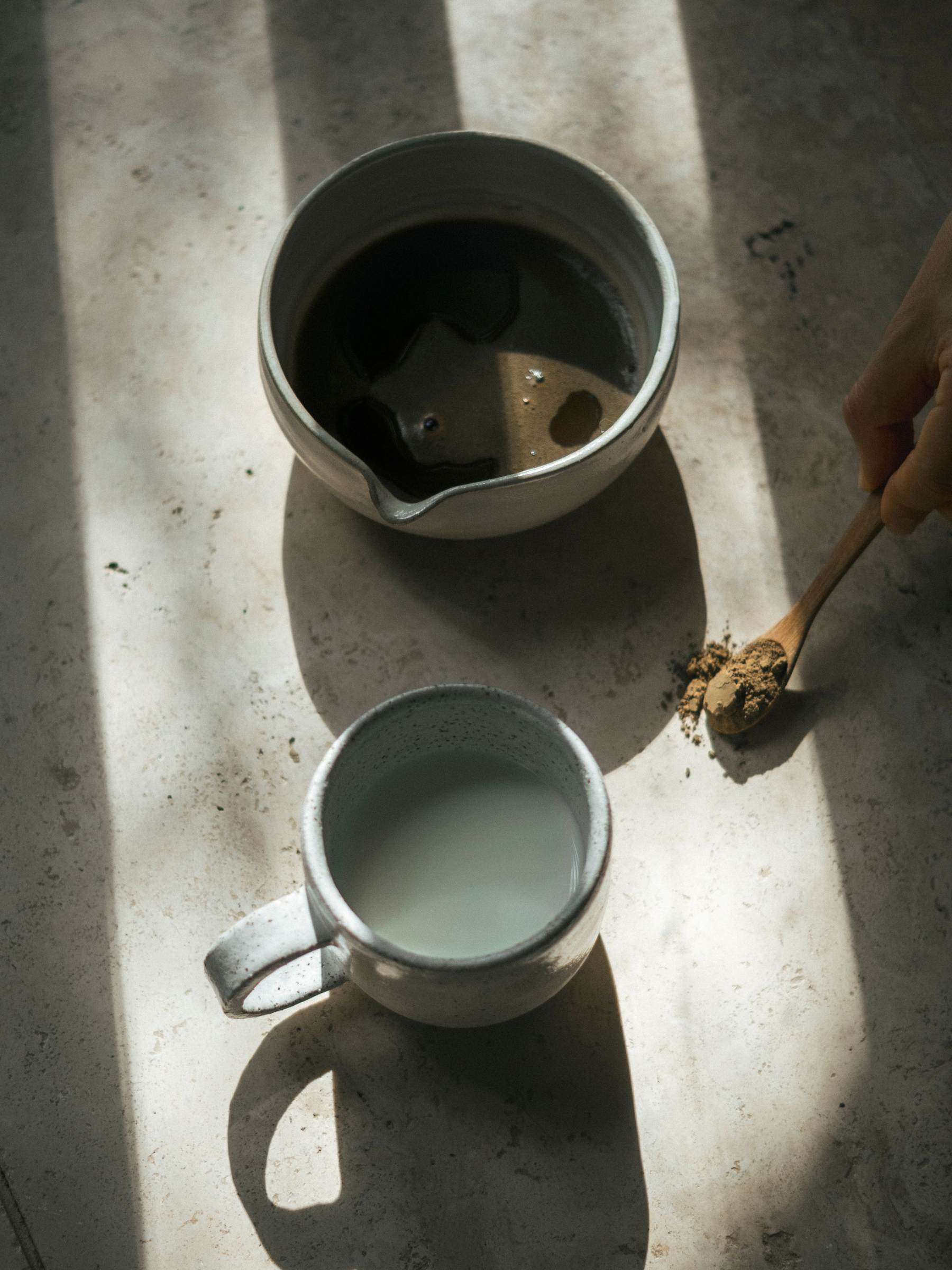 Matcha bowl and mug on a textured surface with a spoon holding hojicha powder.