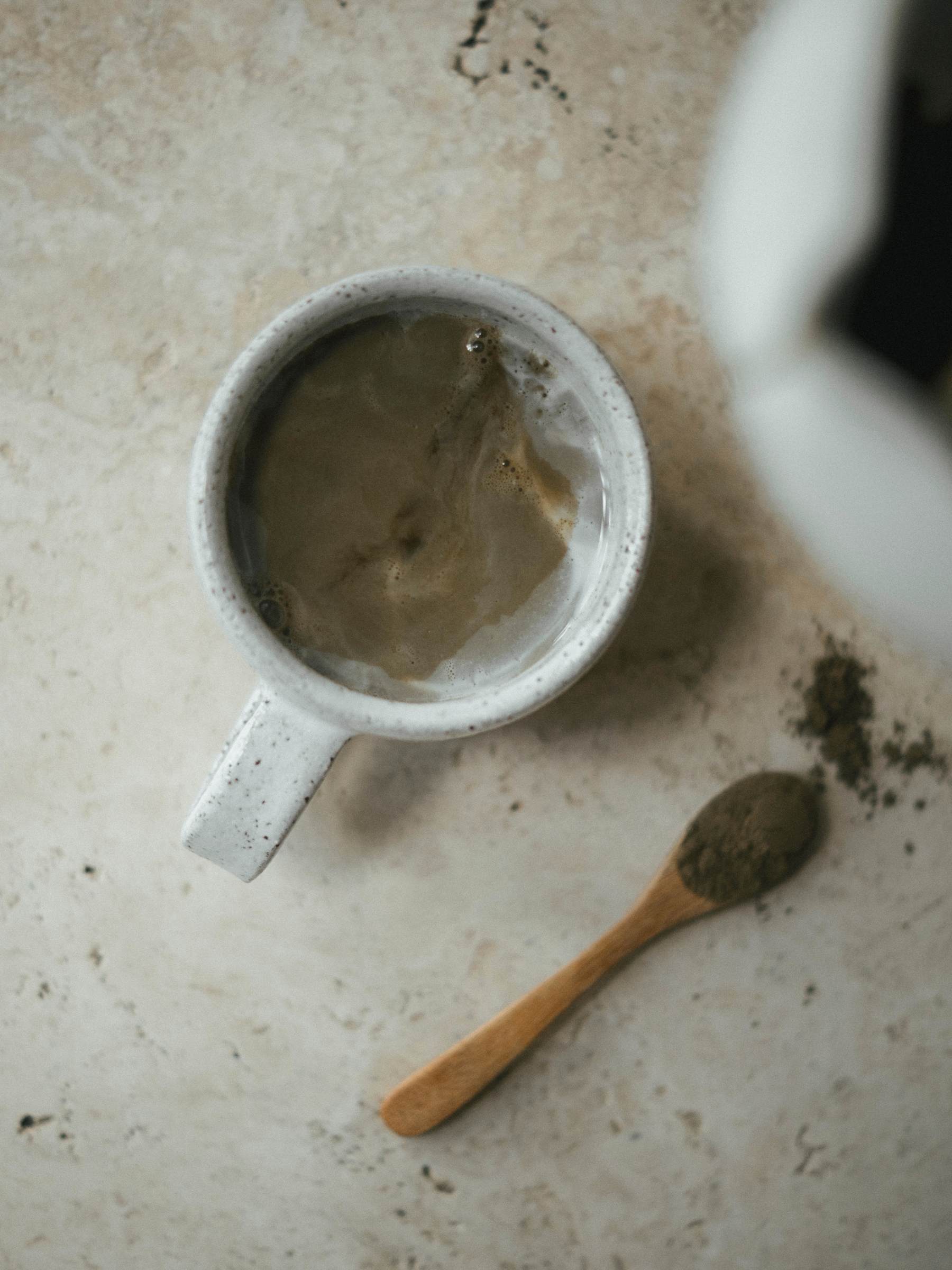 Mug with a hojicha latte and a wooden spoon on a textured surface