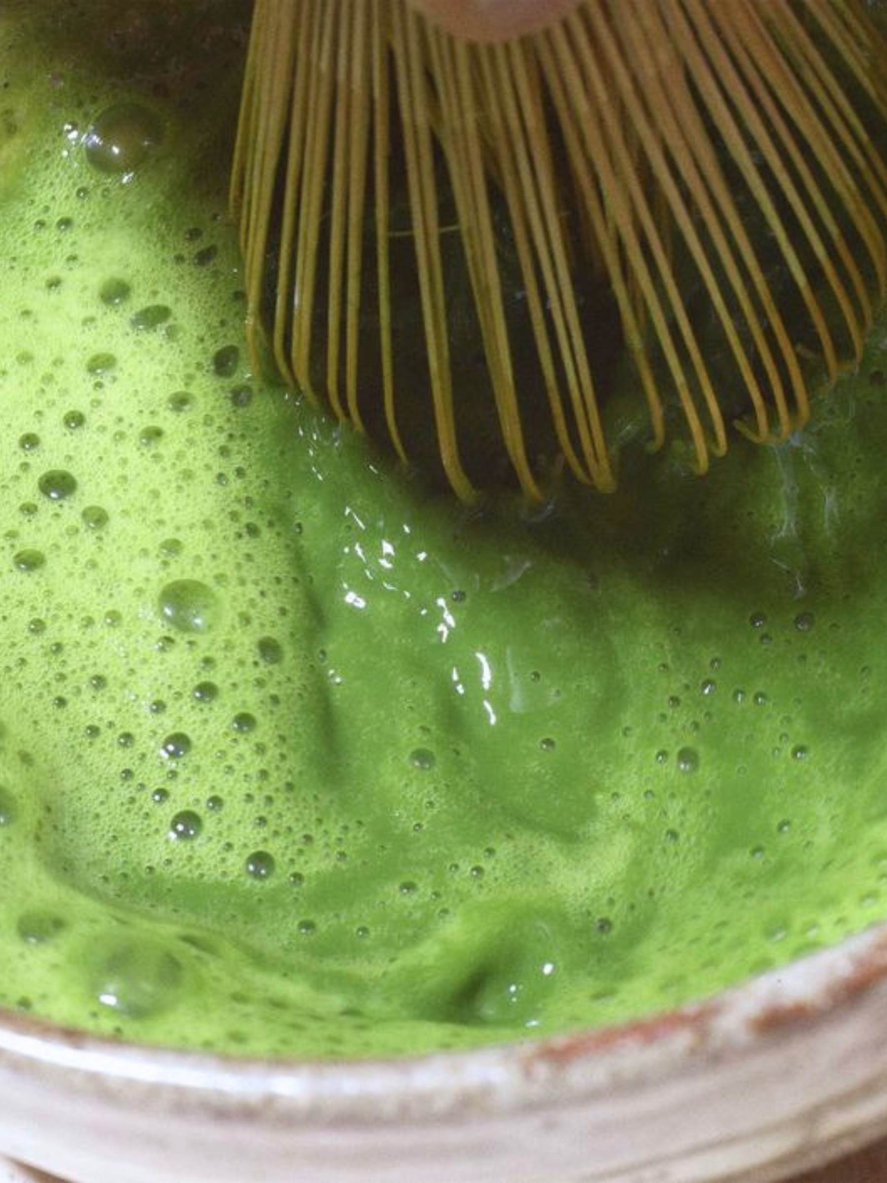 Matcha green tea being whisked with a bamboo whisk in a bowl.