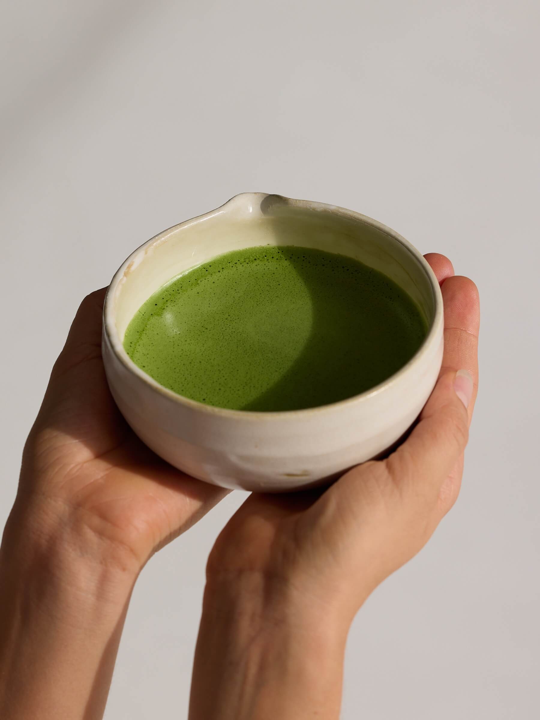 Hands holding a bowl of green matcha tea against a plain background